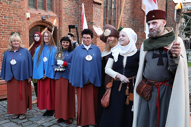 Uczestnicy Jarmarku św. Jakuba w historycznych strojach przed ceglanym budynkiem.