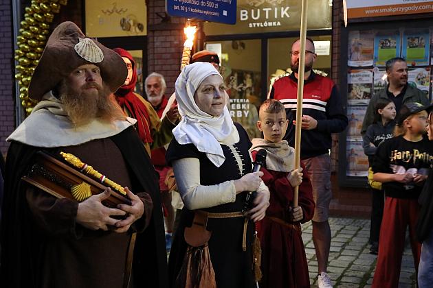 Historyczny pochód z pochodnią i postaciami w dawnych strojach na jarmarku.