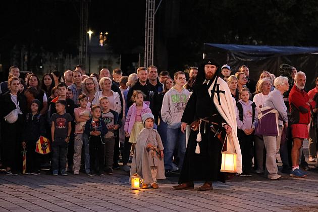 Tłum ludzi i postać w historycznym stroju z lampionem na Jarmarku św. Jakuba.