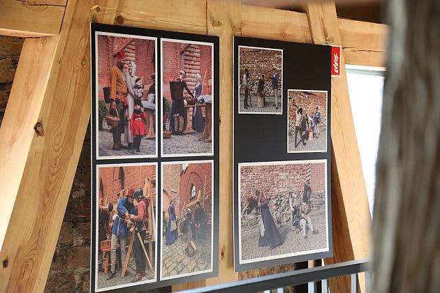 Wystawa historycznych ilustracji i plakatów na drewnianym stelażu.