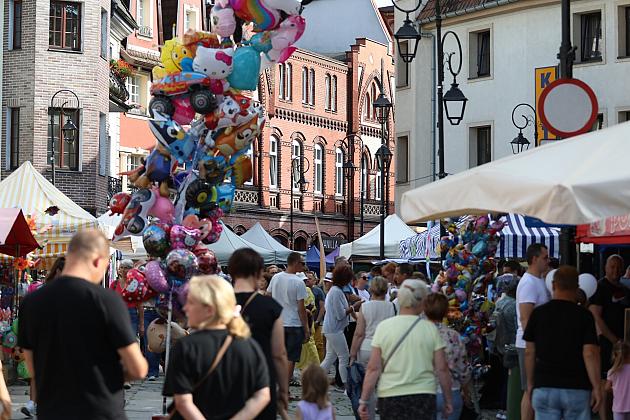 Ulica pełna ludzi, straganów i kolorowych balonów na tle zabytkowych budynków.