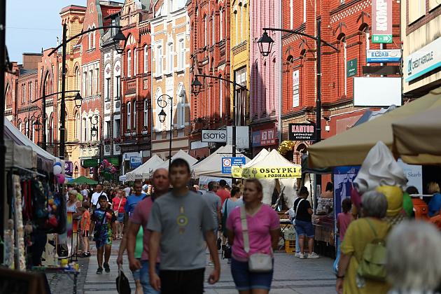 Ludzie spacerujący na jarmarku św. Jakuba pośród stoisk handlowych i kamienic.