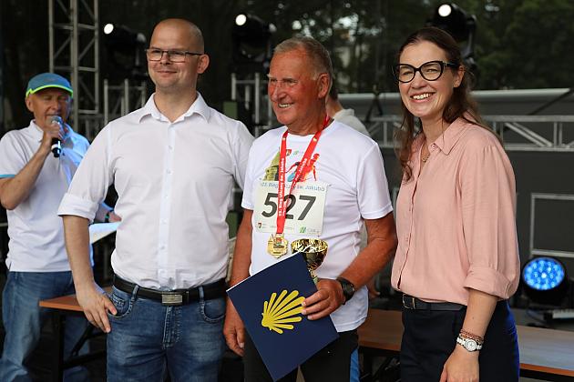 Biegacz z medalem św. Jakuba pozuje do zdjęcia w towarzystwie dwóch osób.