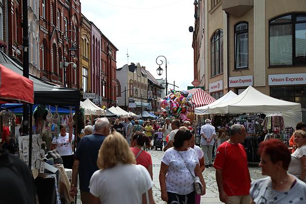 Tłumy ludzi spacerujące między białymi stoiskami na ulicznym jarmarku.