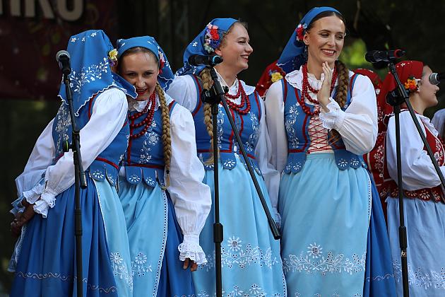 Dziewczęta w niebieskich strojach ludowych śpiewają na scenie jarmarku.