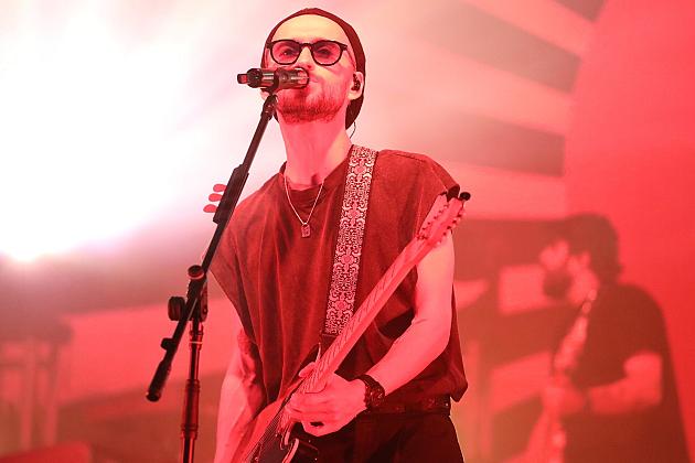 Muzyk gra na gitarze i śpiewa na scenie w czerwonym świetle.