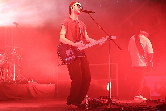 Wokalista gra na gitarze na czerwono oświetlonej scenie Jarmarku św. Jakuba.