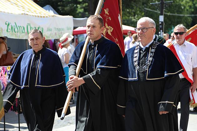 Uroczysty pochód mężczyzn w tradycyjnych togach ze sztandarem na Jarmarku św. Jakuba.