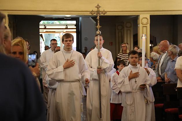 Ministranci idą w procesji z krzyżem i świecą przez kościół.