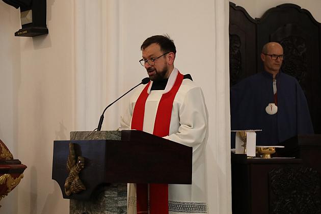 Ksiądz w albie z czerwoną stułą przemawia przy ambonie.