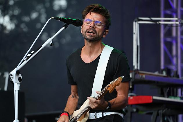 Mężczyzna grający na gitarze i śpiewający do mikrofonu na scenie.