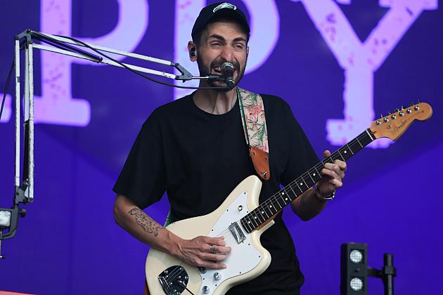 Mężczyzna w czapce gra na gitarze na fioletowym tle.